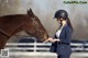 A woman in a blue jacket and helmet petting a brown horse.