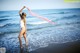 A woman in a white bathing suit standing on the beach.