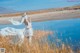 A woman in a white dress standing in tall grass near a lake.