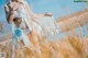A woman in a white bikini standing in a field of tall grass.