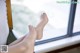 A woman's bare feet sitting on a chair by a window.