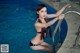 A woman in a blue bikini sitting on the edge of a swimming pool.